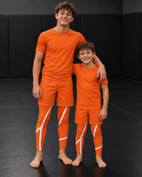 Roll Gear Orange Swirl Spats – Orange/White – Youth, worn by two young athletes in matching sets.