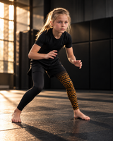 Roll Gear Lion's Pride Kids BJJ Spats – Black & Gold, girl in a low stance on the mat.