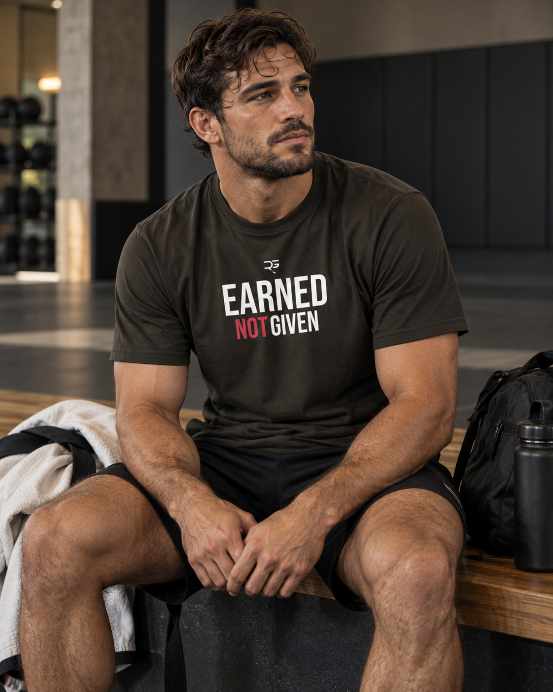 Roll Gear Men’s Earned Not Given T-Shirt, worn seated on a bench with a gym bag.