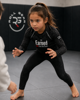Roll Gear Earned Not Given Long Sleeve Rash Guard – Black – Kids, girl in a low stance on the mat.