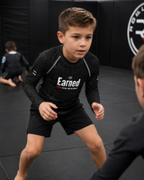 Roll Gear Earned Not Given Long Sleeve Rash Guard – Black – Kids, boy in a ready stance on the mat.