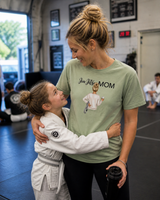 Woman in 'Jiu Jitsu Mom' t-shirt hugging a child in a martial arts uniform in a gym.