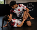 Roll Gear Shadow Dragon Warrior Rash Guard – White & Crimson – Adult Short Sleeve, worn by two athletes drilling on the mat.