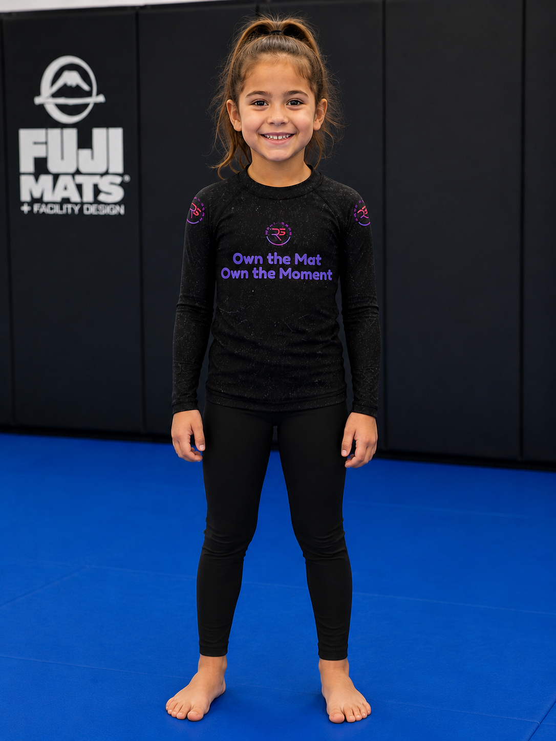 Roll Gear Evolve or Repeat Kid Girls Rash Guard – Black, front view, worn by a smiling young athlete on the mat.