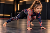 Roll Gear Shadow Dragon Warrior Rash Guard – Dark Navy & Crimson – Kids Long Sleeve, girl stretching in a lunge on the mat.