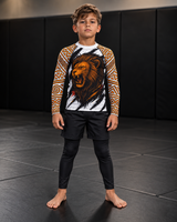 Roll Gear Lion’s Pride Long Sleeve Rash Guard – White & Gold – Kids, front view on a boy, lion chest graphic.