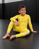 Roll Gear Yellow Swirl Spats – Yellow/White – Kids, boy sitting on the mat in the matching rash guard.