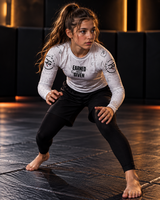 Roll Gear Kids Long Sleeve Rash Guard with White Lines, worn by a girl in a grappling stance on the mat.