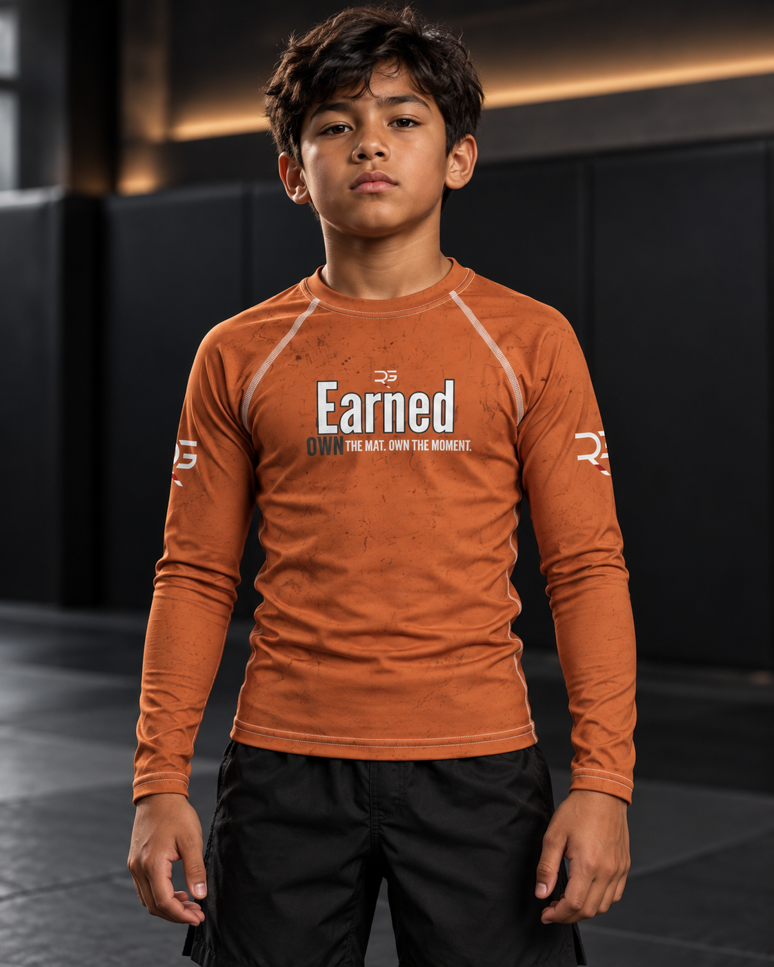 Roll Gear Earned Not Given Long Sleeve Rash Guard – Burnt Orange – Youth, front view on a boy, Earned graphic.