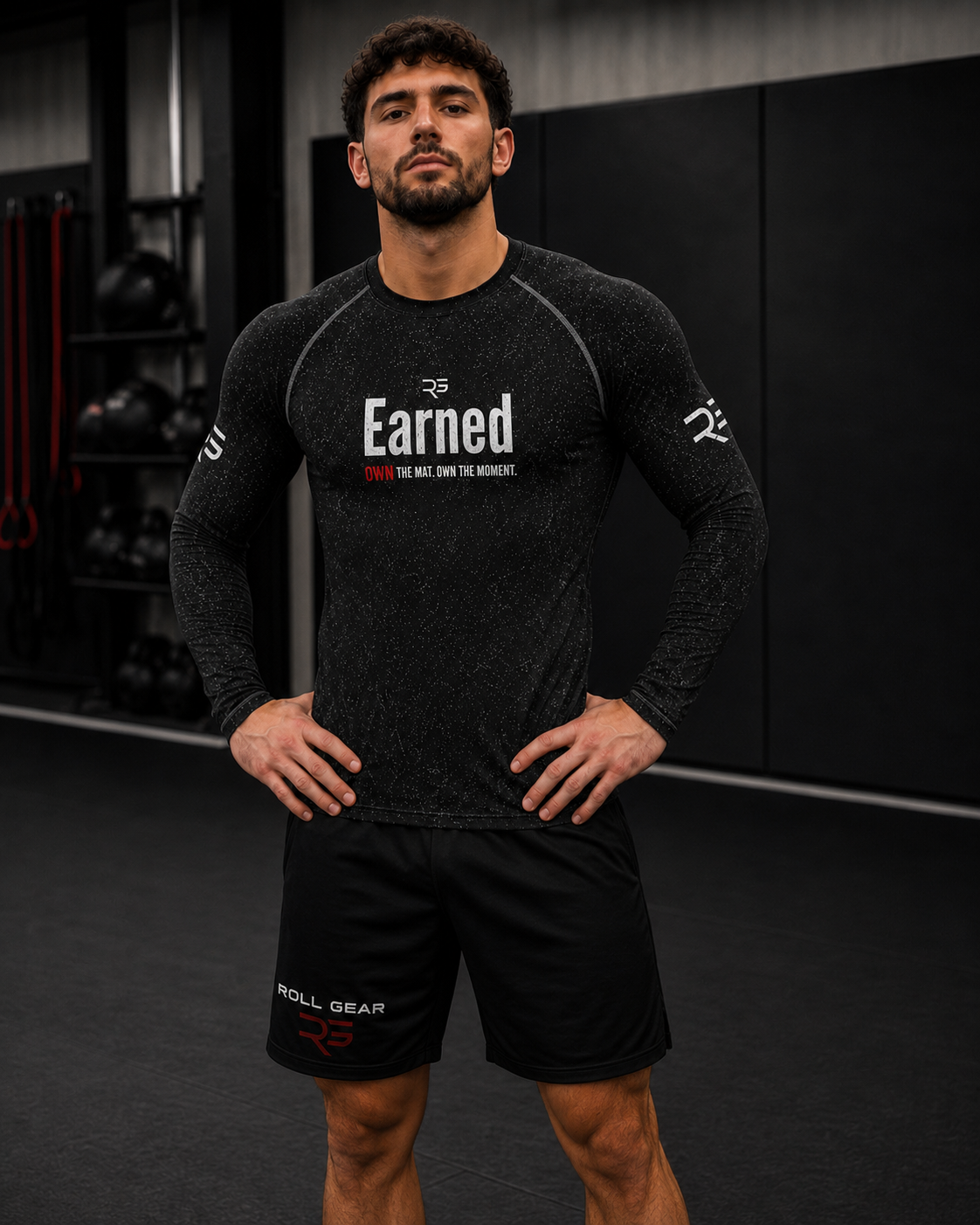 Roll Gear Earned Not Given – Own The Mat Long Sleeve Rash Guard – Men's Black, worn by a model in a gym.