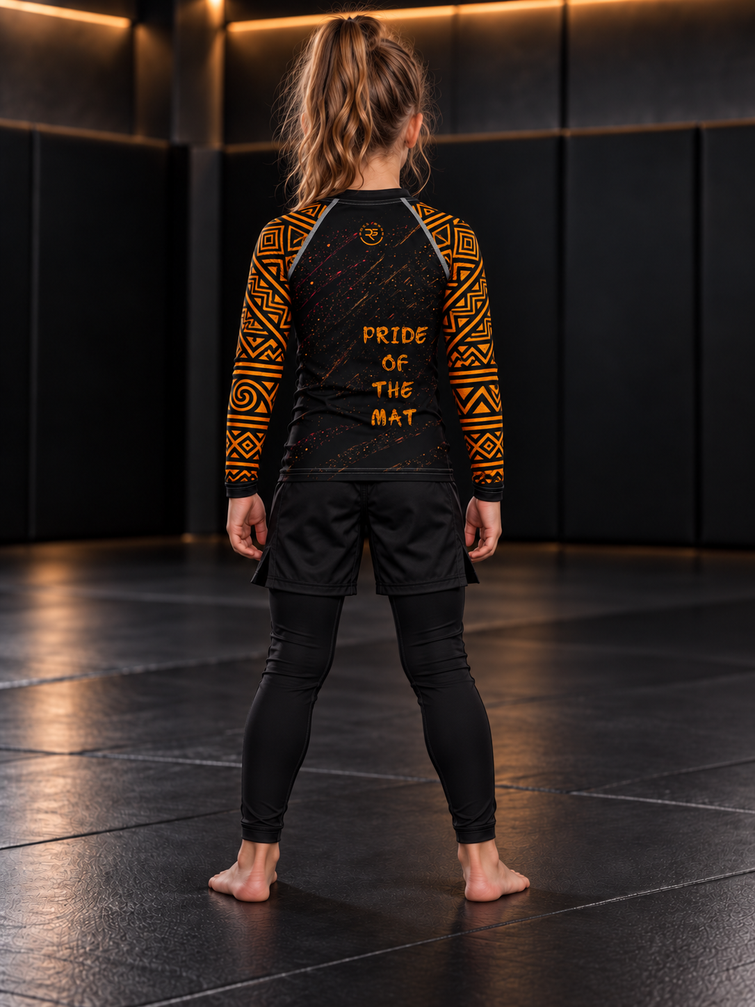 Roll Gear Lion’s Pride Long Sleeve Rash Guard – Black & Gold – Kids, back view on a girl, Pride of the Mat text.