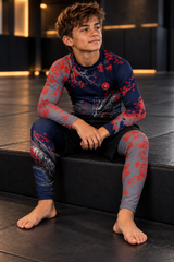 Roll Gear Shadow Dragon Warrior Rash Guard – Youth Long Sleeve, boy seated on a mat step in the matching set.
