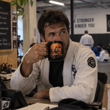 Roll Gear Phantom Pressure Mug, man in a gi drinking from the mug at a desk in an academy.