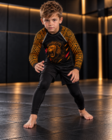 Roll Gear Lion’s Pride Long Sleeve Rash Guard – Black & Gold – Kids, worn by a boy in a grappling stance, lion graphic.