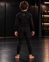 Roll Gear Embrace the Chaos Rash Guard – Kids, back view on a boy standing on the mat.