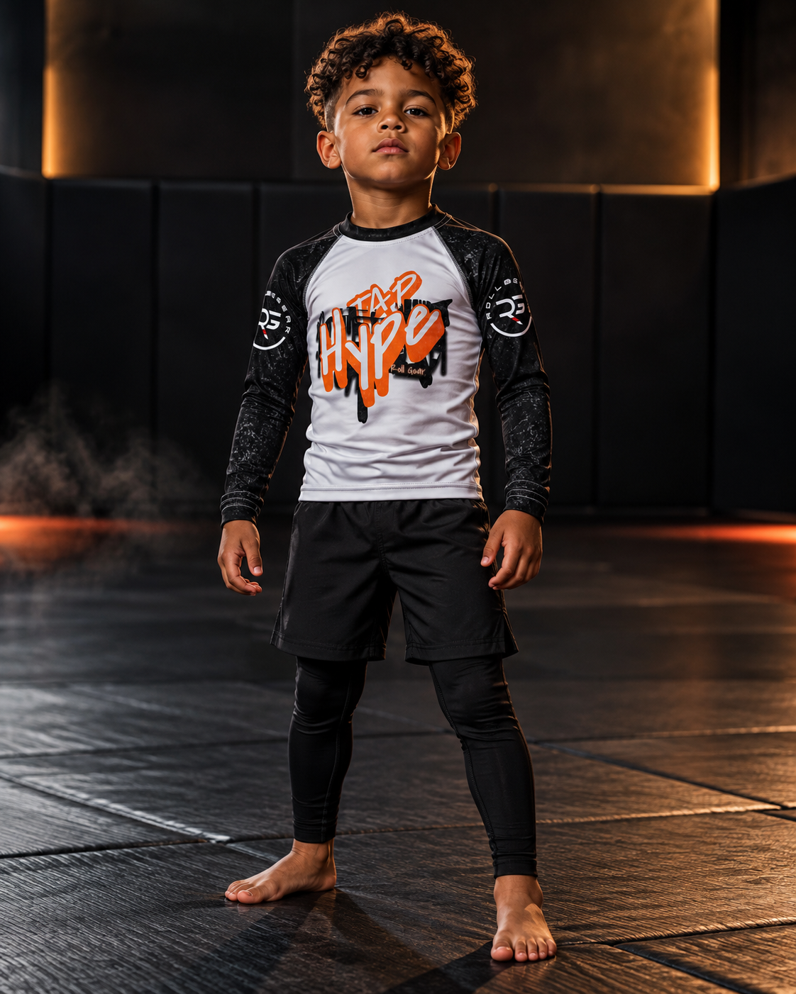 Roll Gear Tap Hype Long Sleeve Rash Guard – Orange & White – Kids, front view on a boy standing on the mat.