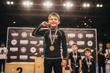 Roll Gear Earned Not Given Long Sleeve Rash Guard – Black – Kids, boy on a tournament podium holding his medal.