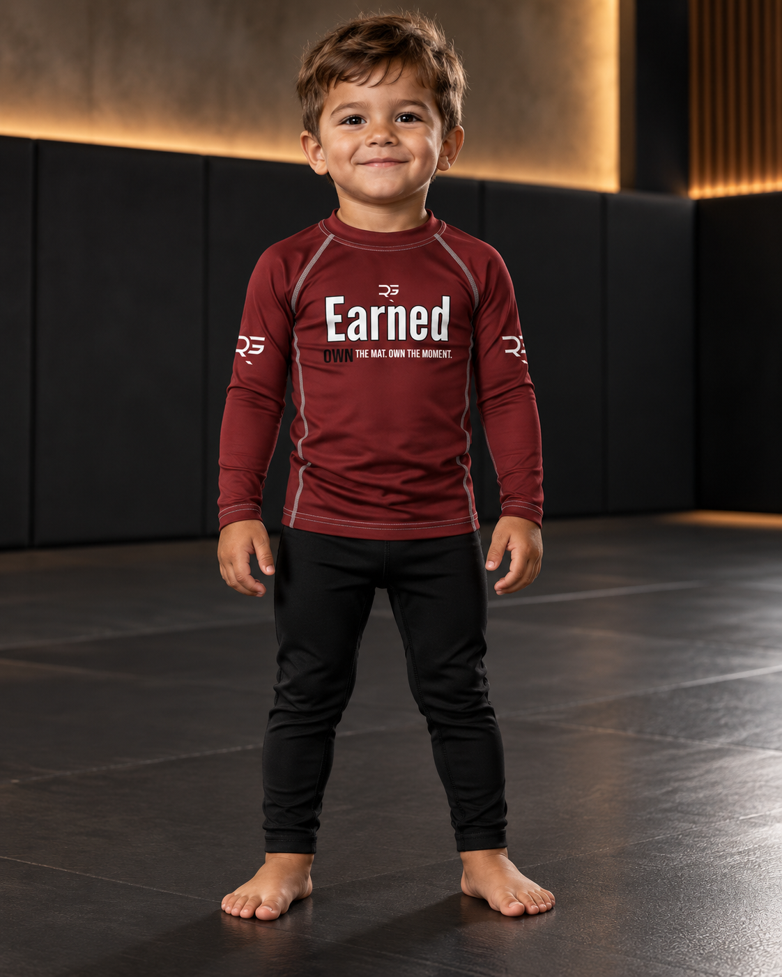 Roll Gear Earned Not Given Long Sleeve Rash Guard – Deep Red – Kids, boy standing on the mat, front view.