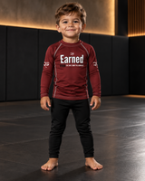Roll Gear Earned Not Given Long Sleeve Rash Guard – Deep Red – Kids, boy standing on the mat, front view.