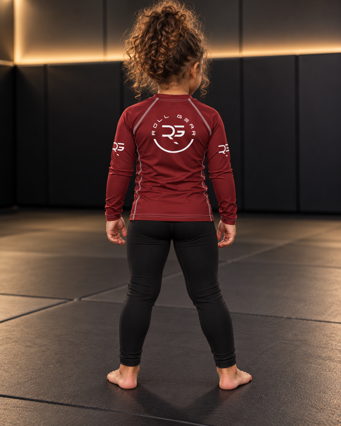 Roll Gear Earned Not Given Long Sleeve Rash Guard – Deep Red – Kids, girl standing on the mat, back view.