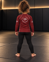 Roll Gear Earned Not Given Long Sleeve Rash Guard – Deep Red – Kids, girl standing on the mat, back view.