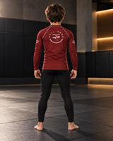 Roll Gear Earned Not Given Long Sleeve Rash Guard – Deep Red – Youth, boy standing on the mat, back view.