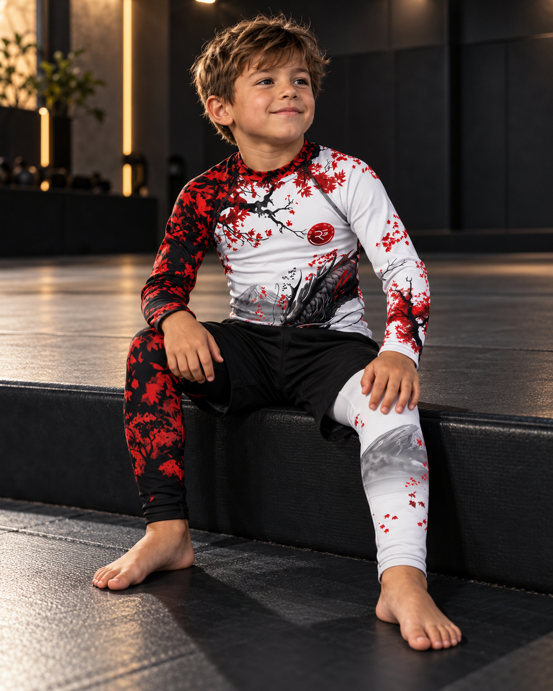 Roll Gear Shadow Dragon Warrior Rash Guard – White & Crimson – Kids Long Sleeve, boy seated on a gym bench.