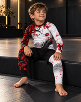 Roll Gear Shadow Dragon Warrior Rash Guard – White & Crimson – Kids Long Sleeve, boy seated on a gym bench.