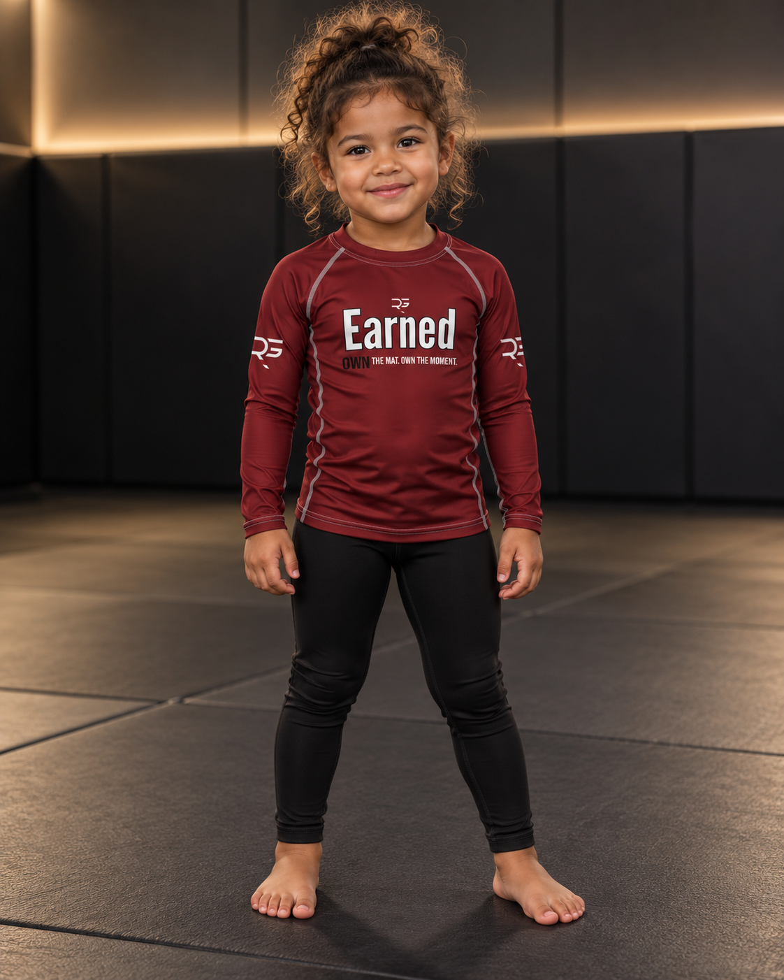 Roll Gear Earned Not Given Long Sleeve Rash Guard – Deep Red – Kids, girl standing on the mat, front view.