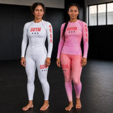 Two women stand in a gym wearing long-sleeve athletic compression shirts and training shorts.