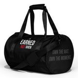 Black polyester duffel bag by Roll Gear with "EARNED NOT GIVEN" graphic and "OWN THE MAT. OWN THE MOMENT." text.