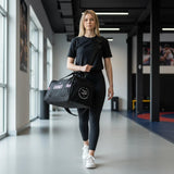 Black polyester duffel bag with Earned Not Given text and Roll Gear logo, carried by a woman in athletic wear.