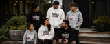 Six people wearing matching custom-printed hoodies with the text 'EARNED NOT GIVEN' in white, black, and gray, posed outdoors in front of a modern building.