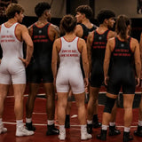 A group of athletes wearing athletic singlets stand together on a track field. The singlets are either white with red trim and red text reading 'OWN THE MAT.