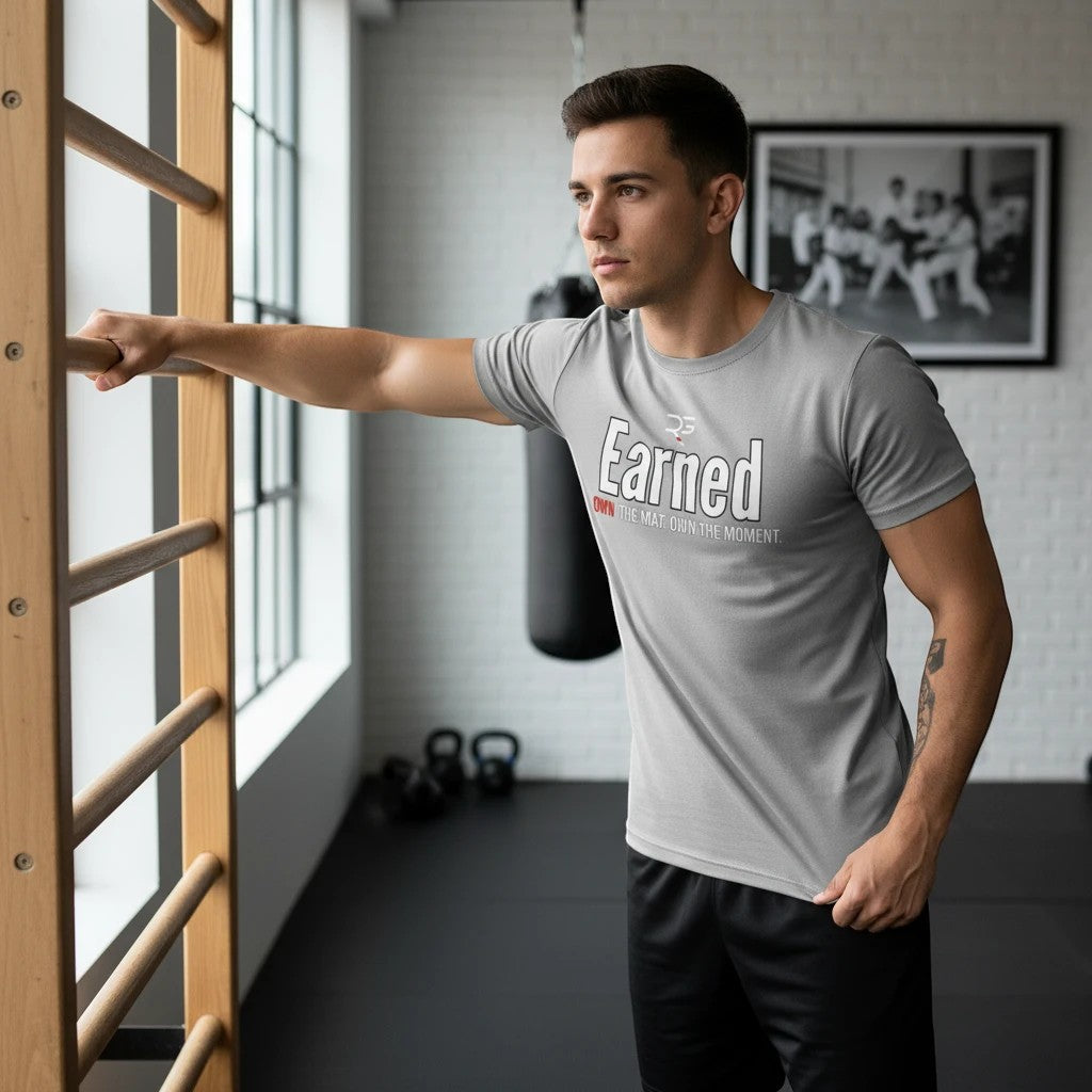 Roll Gear grey cotton t-shirt with "Earned Not Given" graphic print, short sleeves, crew neck, worn by a man in a gym.