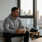 Roll Gear Earned Not Given Legacy Edition grey cotton blend hoodie with graphic text on chest. Man sitting on couch holding mug.