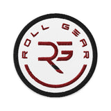 Roll Gear circular embroidered patch with RG logo in red on white, red border, and black edge. Cotton-polyester blend.