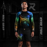 A man stands in a dark gym wearing a long-sleeve black rash guard with a colorful cosmic spiderweb graphic and the word 'PREDATOR' across the chest, paired with matching black shorts. Background shows punching bags and padded gear with 'ROLL GEAR' text.