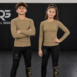 Two models, a man and a woman, wearing matching tan long-sleeve compression shirts and black leggings with gold USMC graphics, standing on a black mat with a dark background.