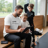 Man seated mat-side with kids, wearing the white Jiu Jitsu Dad tee with the “Full-Time Mat Analyst” front print.