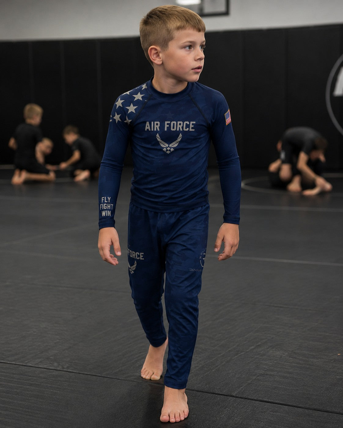 Roll Gear Kids Air Force blue long sleeve rash guard with silver graphics and matching pants, worn by a boy on a mat.