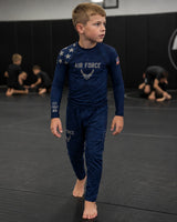 Roll Gear Kids Air Force blue long sleeve rash guard with silver graphics and matching pants, worn by a boy on a mat.