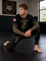 Roll Gear Kids Marines “Gold” military rash guard in black with faded gold sleeves and USMC emblem. Compression fit, long sleeve.