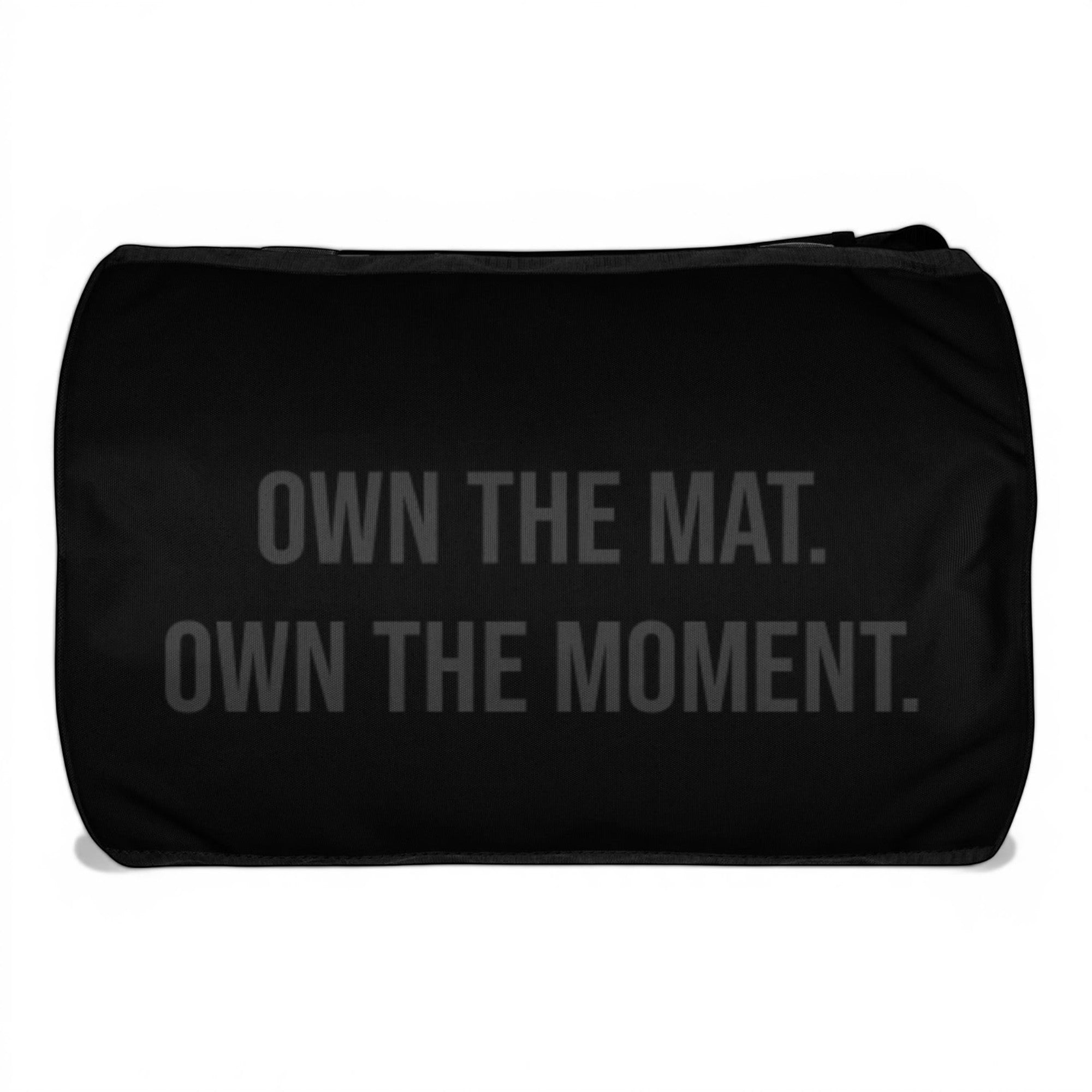 Roll Gear LLC black polyester cylinder duffel bag with "OWN THE MAT. OWN THE MOMENT." graphic.