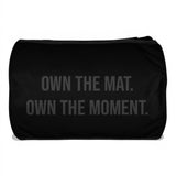 Roll Gear LLC black polyester cylinder duffel bag with "OWN THE MAT. OWN THE MOMENT." graphic.