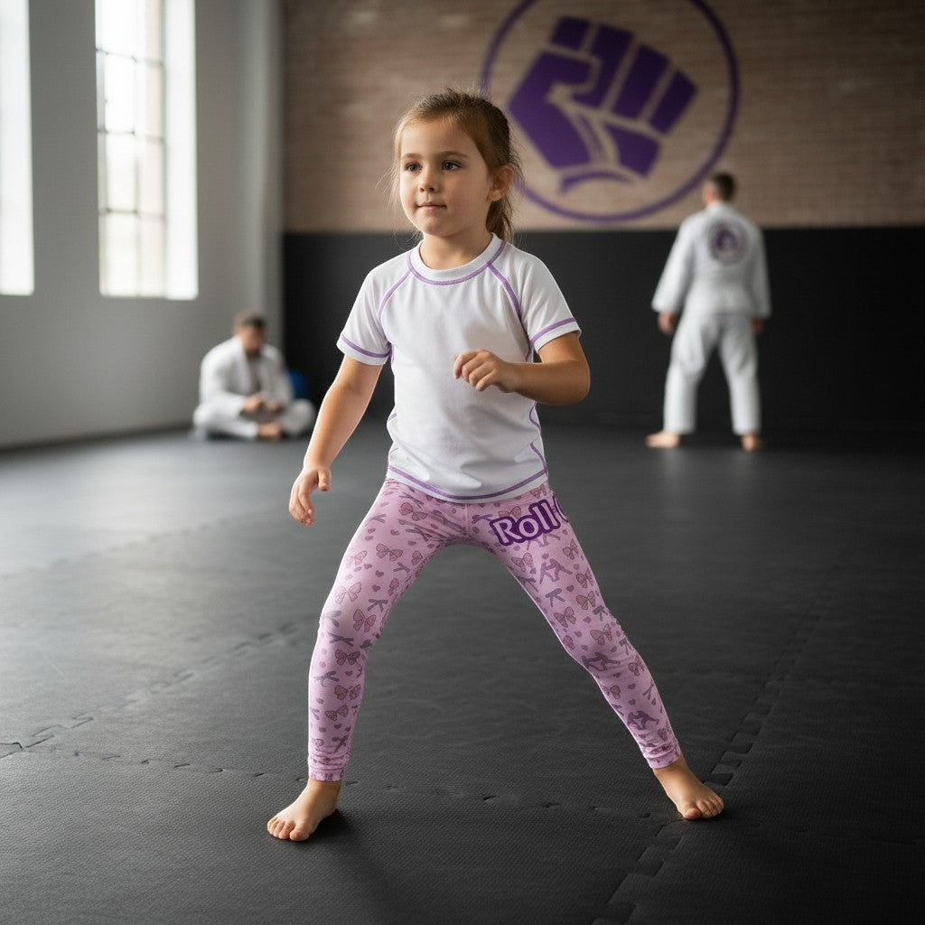 Roll Gear Girls Bow Kids BJJ Spats – Pink, girl standing in an academy.