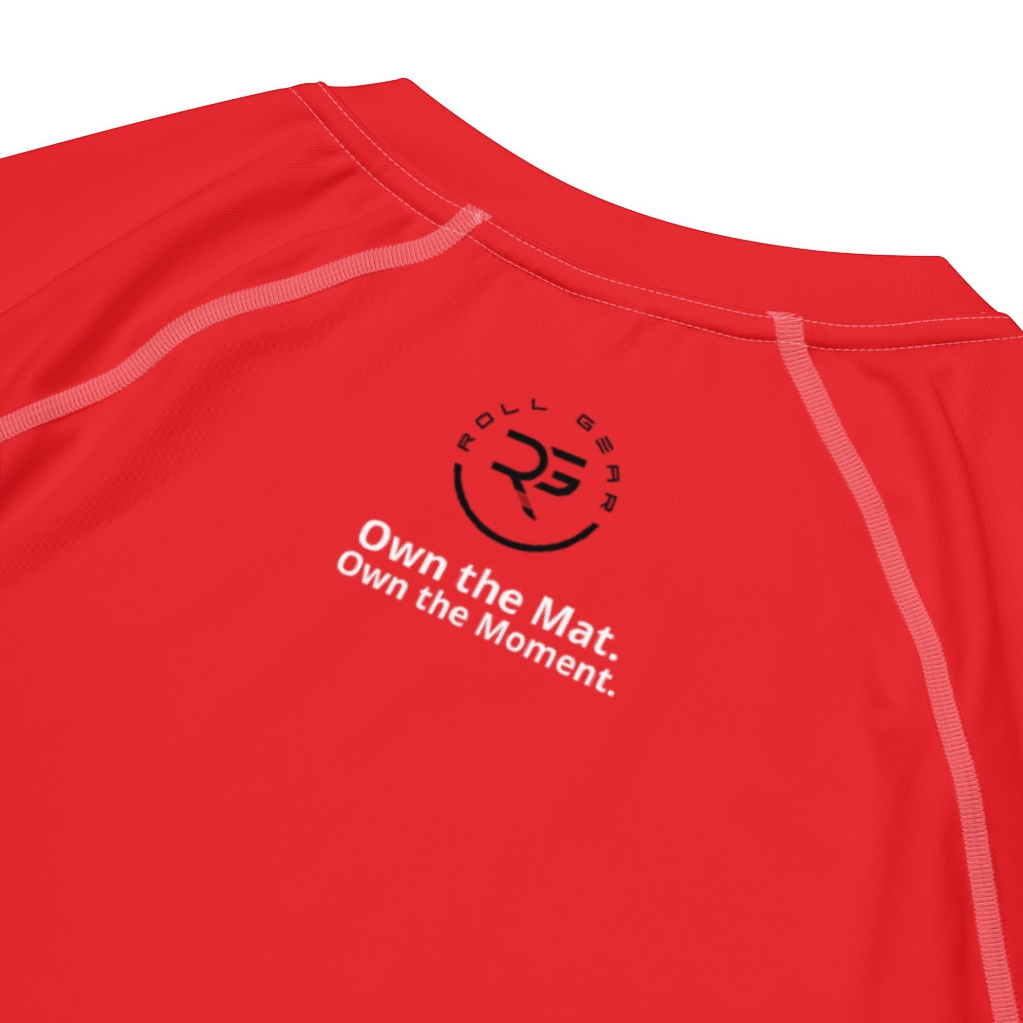 Roll Gear Performance Rash Guard – All Red Edition, close-up of the Roll Gear emblem and Own the Mat text.