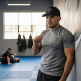 Roll Gear black trucker cap with embroidered logo, mesh back, and structured front panels. Worn by a man in a grey t-shirt.