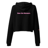 Roll Gear Women's black cropped hoodie with pink text 'Own the Moment.' on back. Ribbed cuffs and hem.