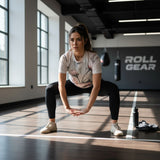 Roll Gear Athlete Edition women's short sleeve rash guard with floral print, black leggings, and white sneakers performing a squat.